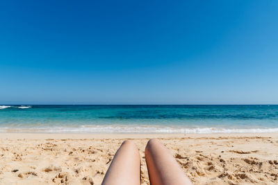 Low section of woman on beach against clear blue sky