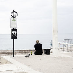 Rear view of woman sitting on seat by sea against sky