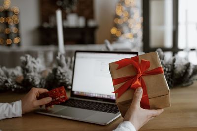 Cropped image of person holding gift and credit card while using laptop