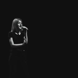 Young woman singing against black background