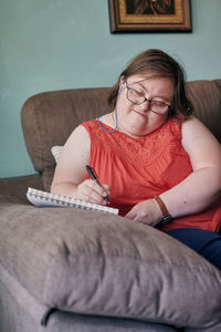 Adult woman with down syndrome writes in a notebook on a couch at home