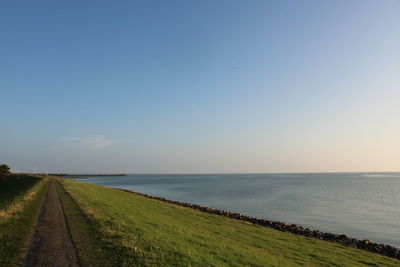 Scenic view of road by sea against clear sky