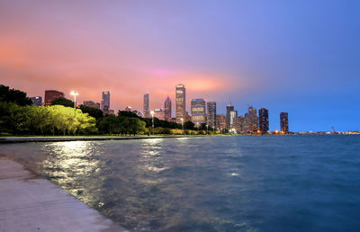 Sea by city buildings against sky during sunset