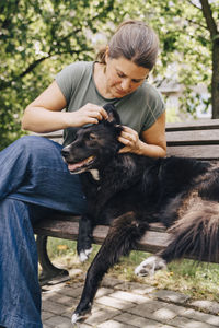 Mature woman examining dog's ear while sitting on bench in park