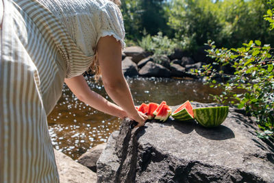 Midsection of woman cutting watermelon by river