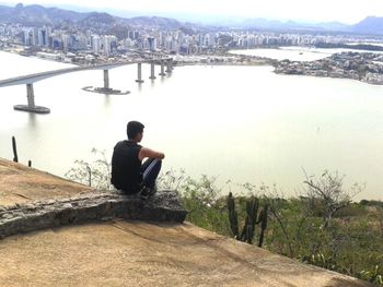 Man sitting on bridge over river in city