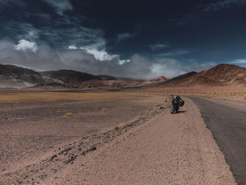 Rear view of man walking on dirt road against sky
