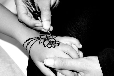 Midsection of person applying henna tattoo on child hand