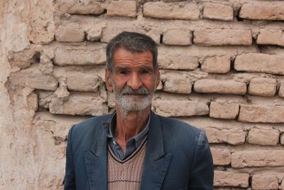 Portrait of senior man standing against brick wall