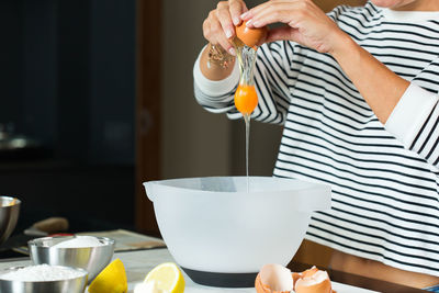 Woman breaking eggs while cooking apple pie in the modern kitchen