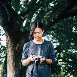 Young woman photographing while standing on tree