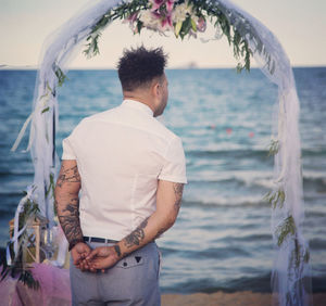 Rear view of man standing at beach against sky