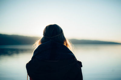 Rear view of woman standing in front of lake against sky