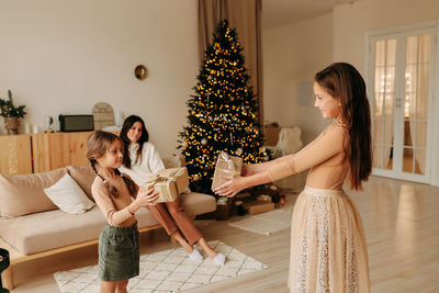 Side view of woman holding christmas tree at home