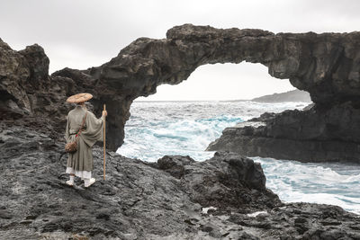 Monk wearing hat standing in front of rock arch