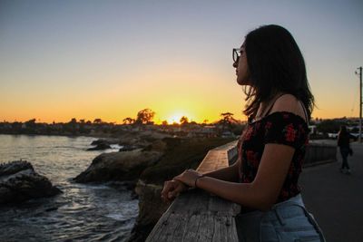 Woman sitting on rock against sea during sunset