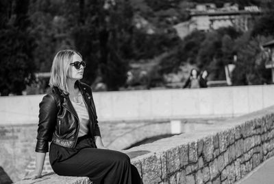 Side view of woman wearing sunglasses while sitting on stone wall