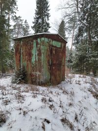 Built structure on snow covered field against trees in forest