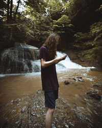 Full length of man standing on rock against waterfall