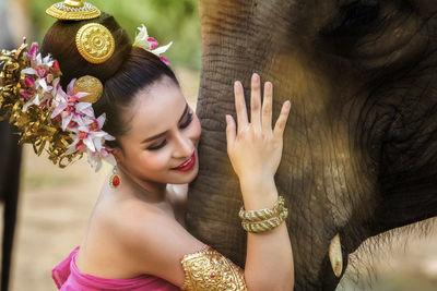 Smiling young woman in traditional clothes holding elephant trunk 
