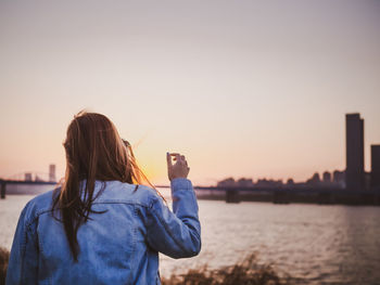 Rear view of woman photographing against sky during sunset