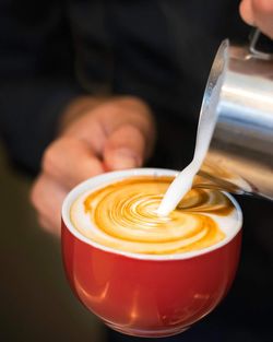 Midsection of barista pouring milk in coffee cup