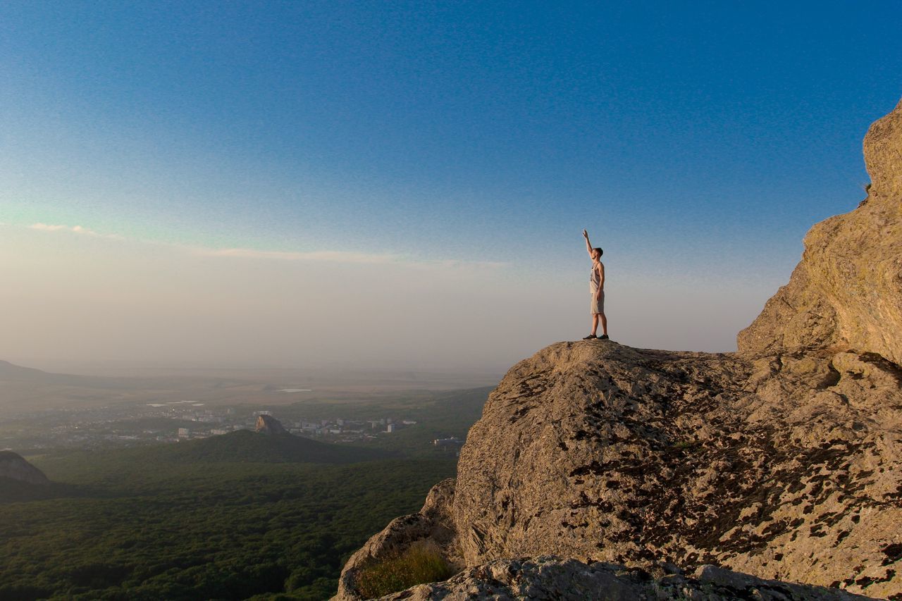 MAN STANDING ON ROCKS AGAINST SKY