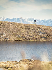 Side view of man riding bicycle on hill by lake