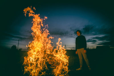 Woman standing by bonfire against sky at night