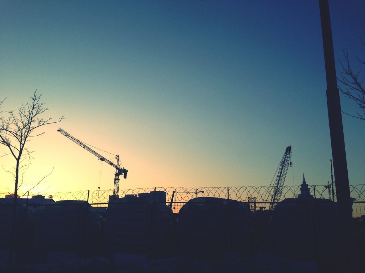 clear sky, silhouette, sunset, built structure, copy space, architecture, building exterior, construction site, low angle view, industry, construction, development, blue, crane - construction machinery, electricity pylon, dusk, crane, fuel and power generation, outdoors, orange color