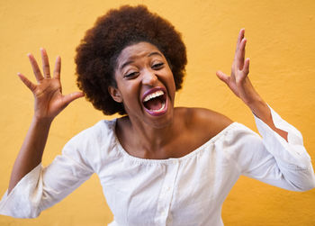 Portrait of angry young woman screaming against yellow wall