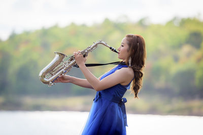 Side view of young bride playing saxophone by lake