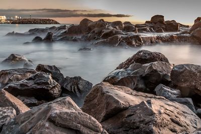 Rocks by sea against sky during sunset