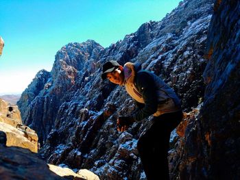 Side view of man on rock against sky