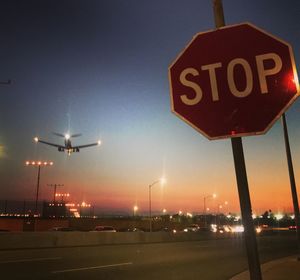 Road sign on street in city against sky during sunset