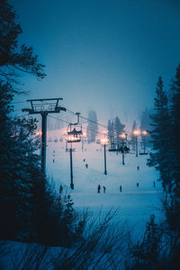 Overhead cable cars hanging by trees against sky