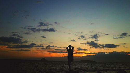 Silhouette woman standing on beach against sky during sunset