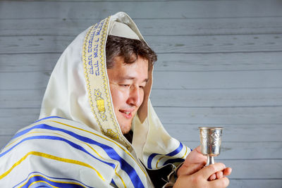 Close-up of smiling priest holding chalice by wall