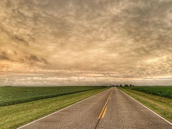 Road amidst field against sky during sunset