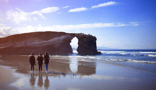 Rear view of women walking at beach against sky