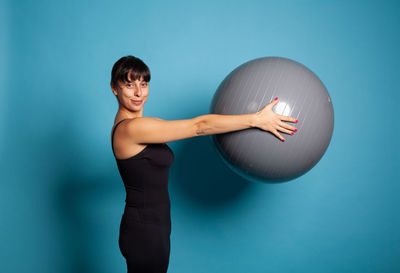 Portrait of young woman exercising against blue background