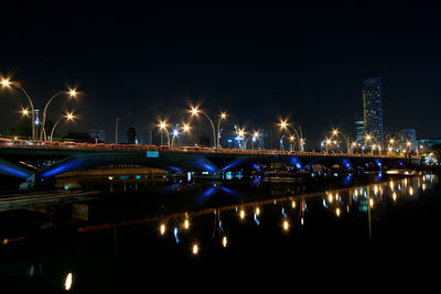 Illuminated bridge over river in city at night