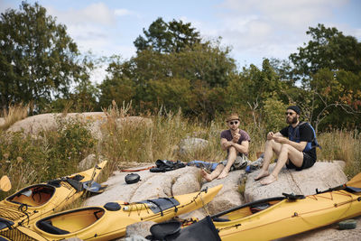 Men sitting at rocks on coast near kayaks