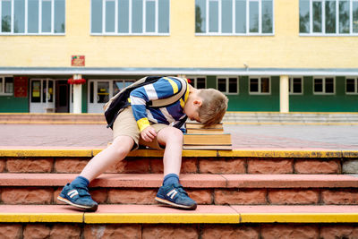 Full length of boy sitting against building