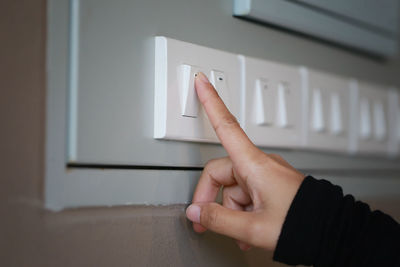 Close-up of human hand pressing switch button in wall