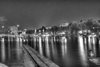 Illuminated city by river against sky at night