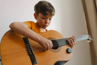 Cute boy learns to play the classical guitar in home. cozy home.