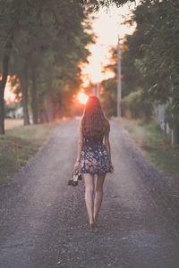 Rear view of woman walking on footpath during sunset