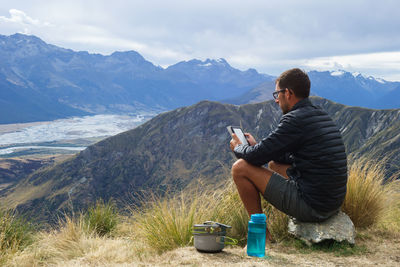Man using mobile phone while sitting on mountain