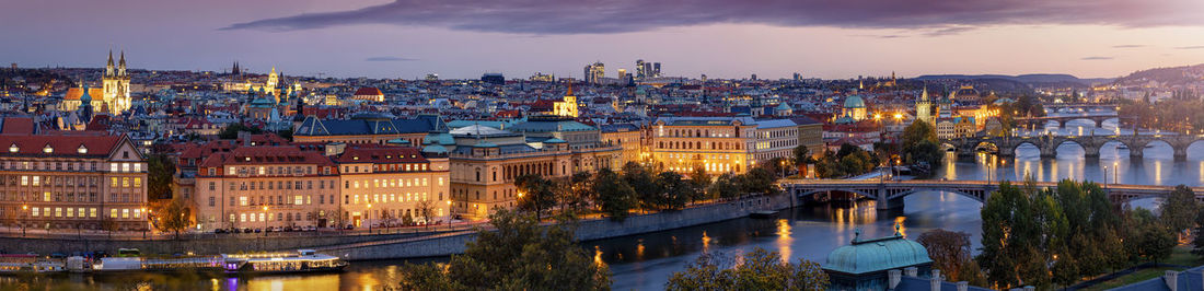 Illuminated cityscape by river against sky at dusk